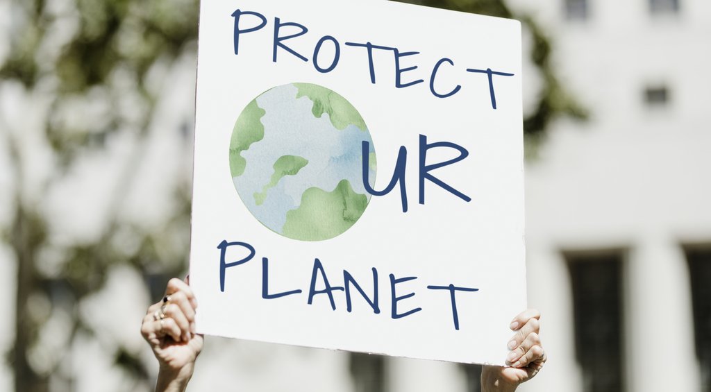 Mãos segurando uma placa com a escrita "Protec ur planet" representando a importância de ações em prol da sustentabilidade. 