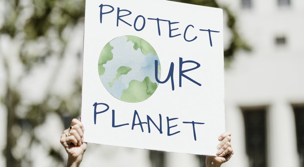 Mãos segurando uma placa com a escrita "Protec ur planet" representando a importância de ações em prol da sustentabilidade.