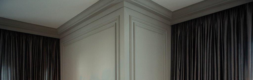 Foto de um espaço residencial com decoração em cores neutras, cinza-escuro e branco, e cheio de detalhes, como boiserie, luminária, vaso e rodateto Santa Luzia