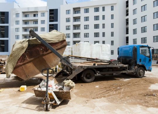 Caminhão poliguindaste descarregando uma caçamba de entulho em uma obra, simbolizando o gerenciamento de resíduos na construção civil.