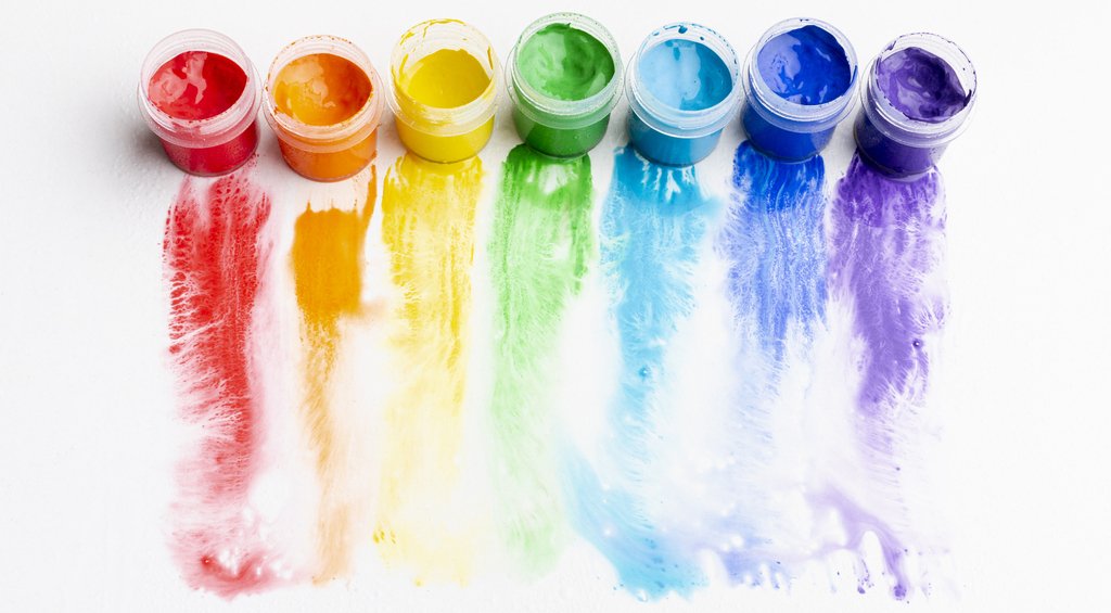 Imagem de 7 potes de tinta aquarela escolar com cores diferentes na parte superior, com suas tintas derramadas no sentido de cima para baixo, simbolizando a psicologia das cores na arquitetura.