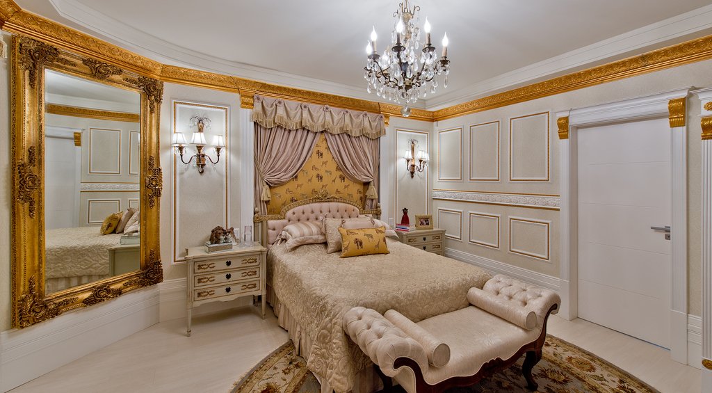 Utilização de molduras boiseries em um quarto com decoração clássica em tons claros e dourados.