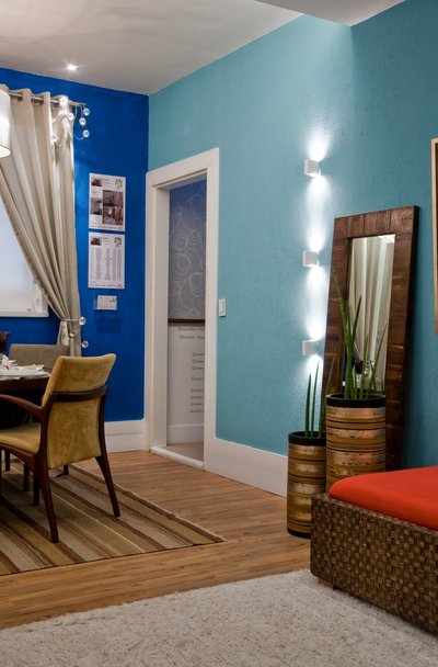 Ambiente decorado em tons claros de azul e marrom. Com uma mesa de jantar, espelho e uma poltrona, exemplificando como decorar uma casa nova.