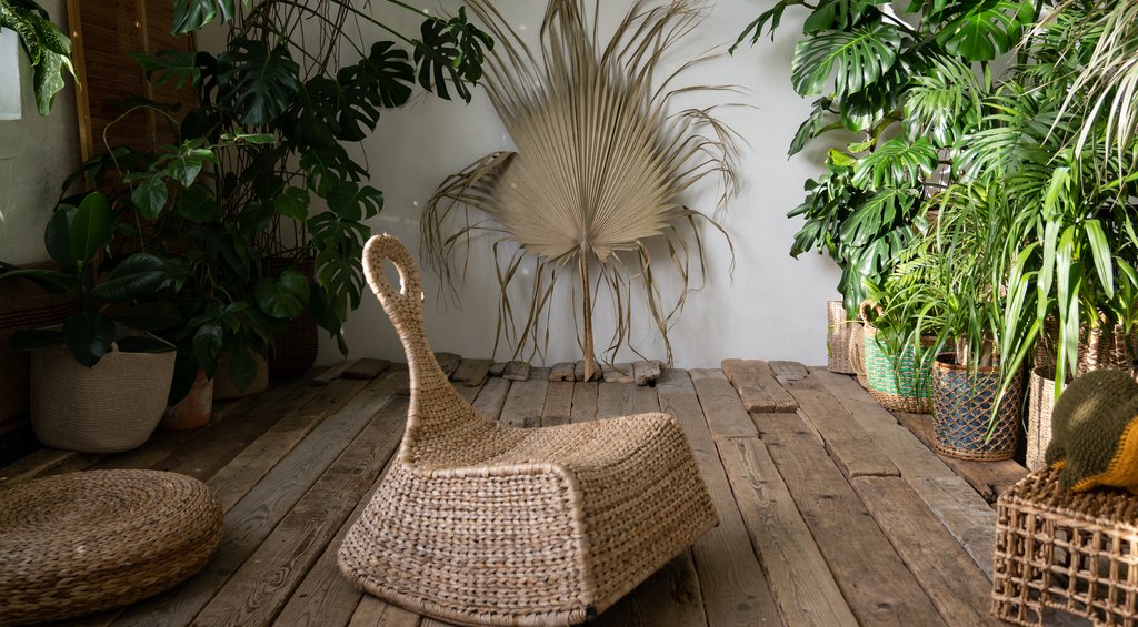 Espaço com elementos de uma decoração zen, como piso em madeira, poltrona feita de material natural, e diversas plantas ao fundo, complementando a decoração.