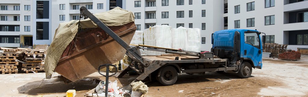 Caminhão poliguindaste descarregando uma caçamba de entulho em uma obra, simbolizando o gerenciamento de resíduos na construção civil.