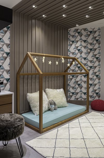 Quarto de criança com decoração em tons de bege e azul. No espaço há uma cama em formato de casa, tapete e revestimento decorativo.