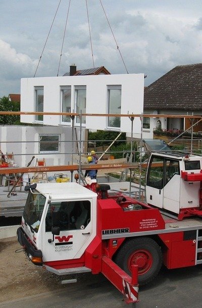 Imagem de um imóvel em construção com um guindaste segurando uma parede, simbolizando as construções modulares.