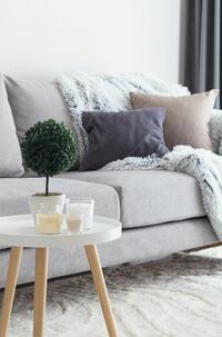 Sala decorada com o estilo comfy com sofá, manta, almofadas, mesinha de centro com objetos, em cores mais neutras e suaves.