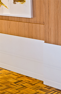 Rodapé branco em uma parede com textura de madeira e decorada com um quadro.