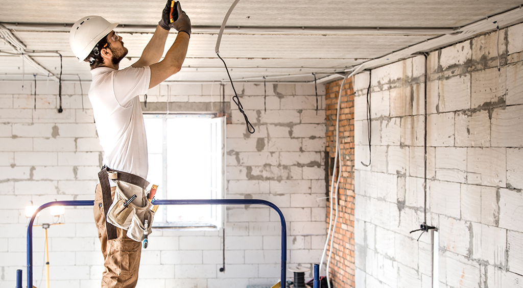 Homem com equipamento de proteção mexendo na parte elétrica, representando a contratação de mão de obra, que é parte da gestão de obras.