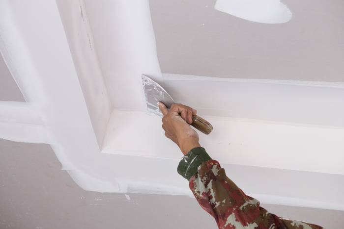 Homem aplicando gesso em uma superfície de drywall.