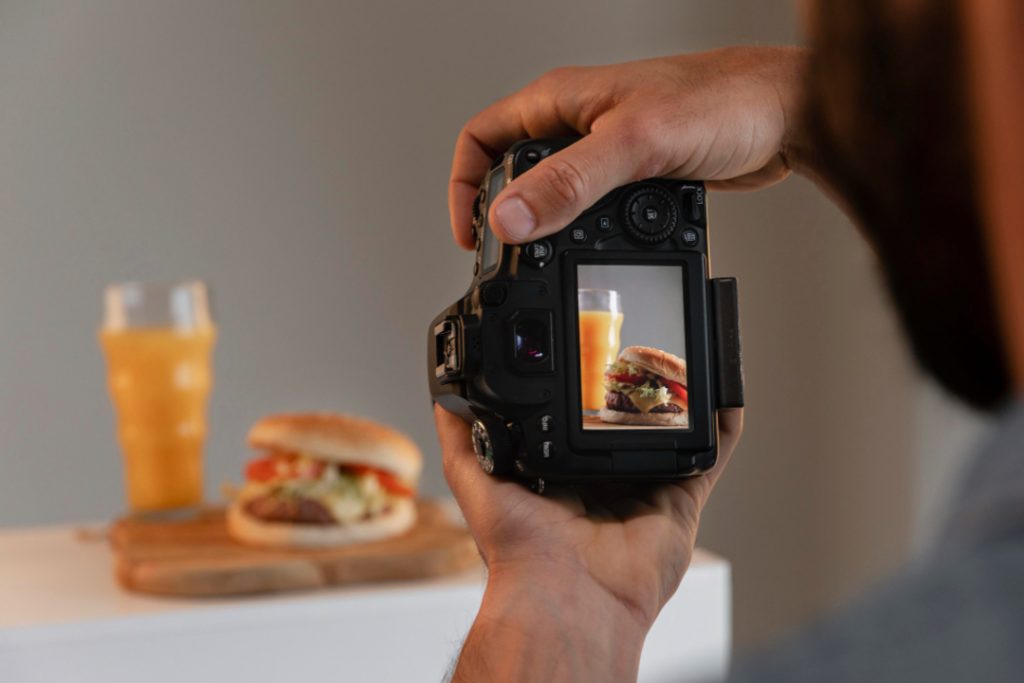 mãos masculinas segurando câmera profissional e ajustando foco para fotografar lanche em uma fotografia de ambiente