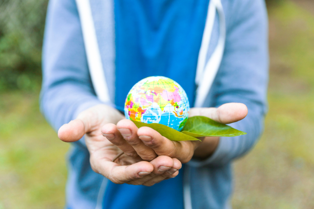 Mão segurando um mini globo terrestre juntamente a uma folha vegetal