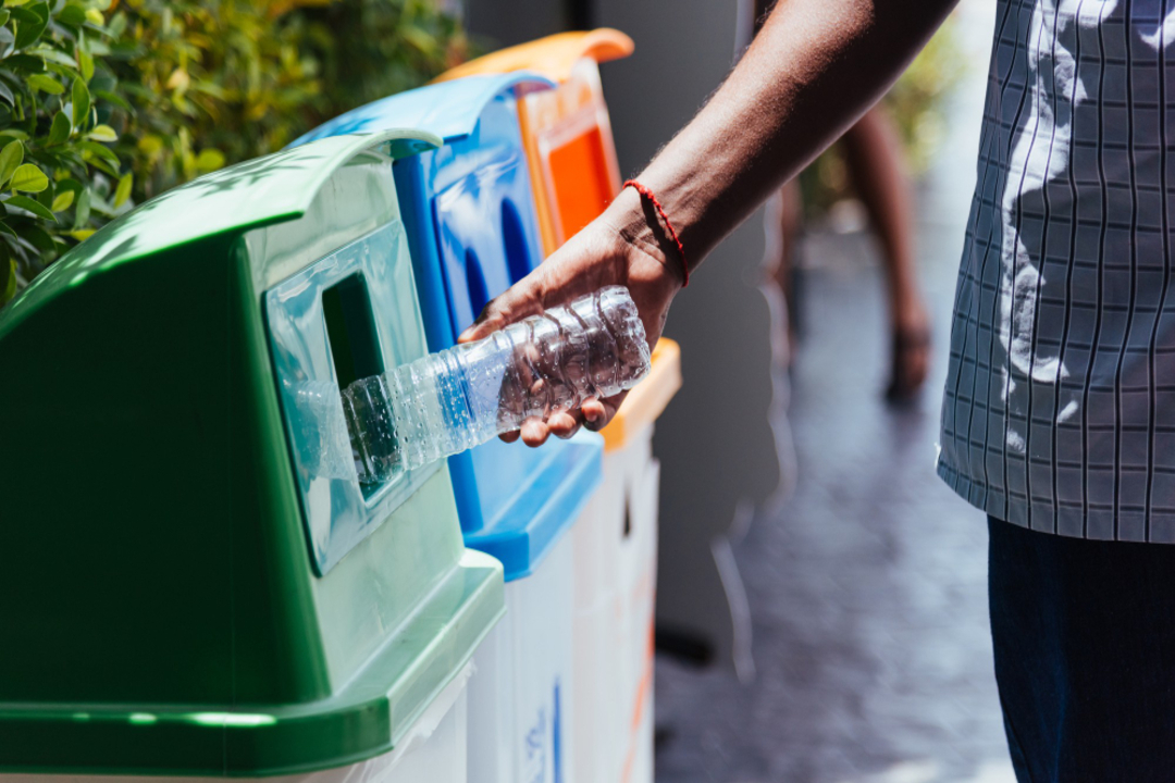 Homem jogando uma garrafa de água no lixo reciclável